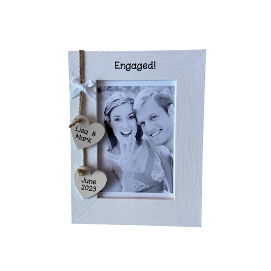 Image shows an engagement photo frame, including two hanging hearts with the names of couple and date of engagement, also a small white bow and bling if wanted.