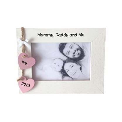 Image shows mummy daddy and baby frame, includes two hanging hearts with baby name and year also a small white bow attached. Bling can be added.