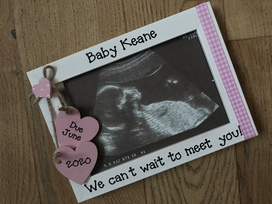 Image shows wooden baby scan photo frame, attached is two hanging hearts with due date, on the other side is gingham ribbon.